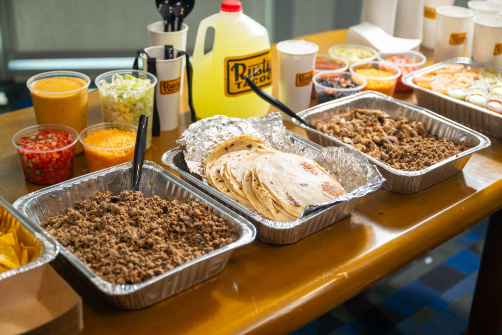 Rusty Taco catering spread with tortillas, taco fillings, toppings, and drinks.